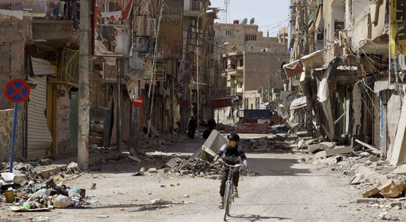 Boy rides his bicycle past damaged buildings in Syria
