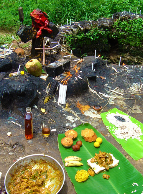 The offering:  Brandy, chicken masala, bananas, ladoos, sliced bread, fried local snacks, jelebis laid out on a banana leaf. I drank the brandy and ate some of the offering. © Mark Ulyseas